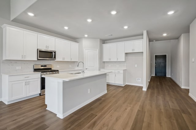 kitchen with appliances with stainless steel finishes, white cabinetry, a kitchen island with sink, and dark hardwood / wood-style flooring