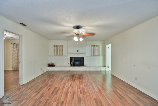 unfurnished living room featuring a fireplace, a textured ceiling, ceiling fan, hardwood / wood-style flooring, and brick wall