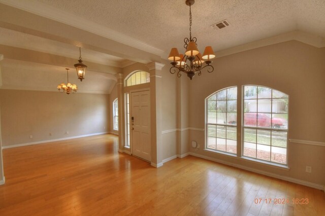 unfurnished room with lofted ceiling, light hardwood / wood-style flooring, a chandelier, and a textured ceiling