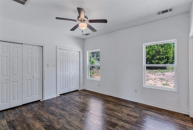 unfurnished bedroom with ceiling fan, dark hardwood / wood-style flooring, and multiple closets