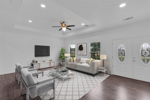 living room featuring ceiling fan, a raised ceiling, and dark wood-type flooring