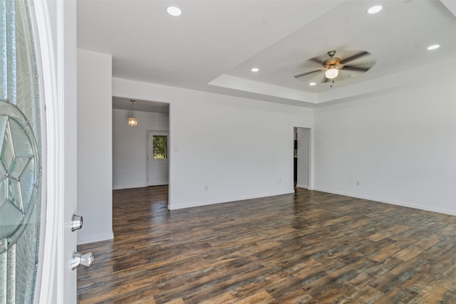 empty room featuring a raised ceiling, ceiling fan, and dark wood-type flooring