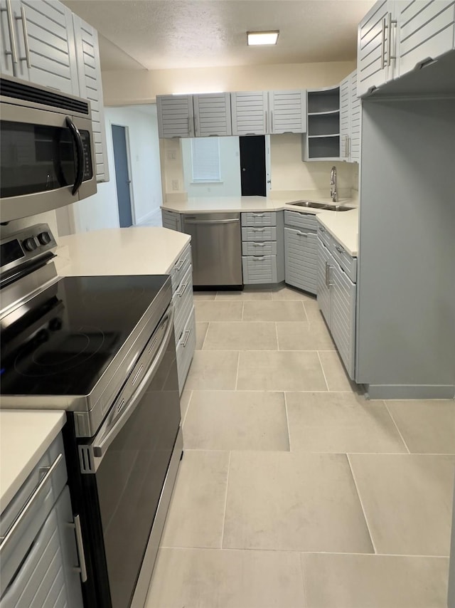 kitchen with a textured ceiling, stainless steel appliances, sink, light tile patterned floors, and gray cabinets