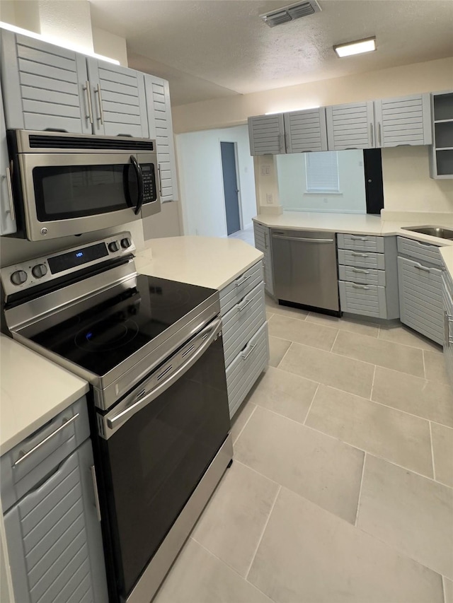 kitchen with gray cabinetry, sink, a textured ceiling, appliances with stainless steel finishes, and light tile patterned flooring