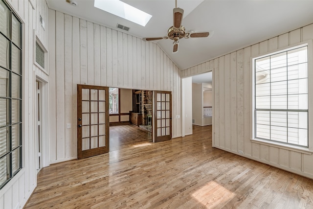 empty room featuring a skylight, french doors, light wood-type flooring, ceiling fan, and high vaulted ceiling