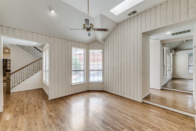 unfurnished living room featuring ceiling fan, vaulted ceiling with skylight, and light hardwood / wood-style floors