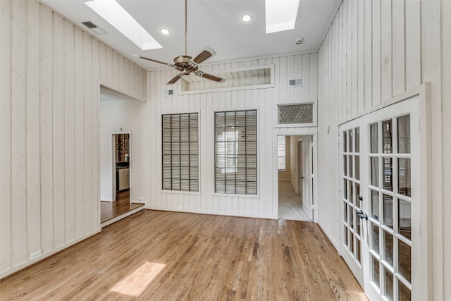 empty room featuring a high ceiling, light wood-type flooring, ceiling fan, and a skylight