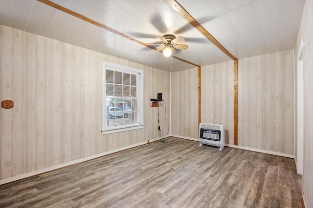 empty room featuring heating unit, a wood stove, wood-type flooring, and ceiling fan