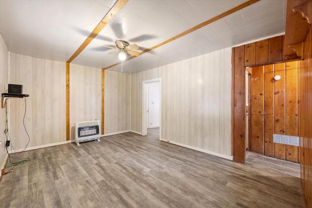 unfurnished living room with hardwood / wood-style flooring, a wood stove, ceiling fan, and wooden walls