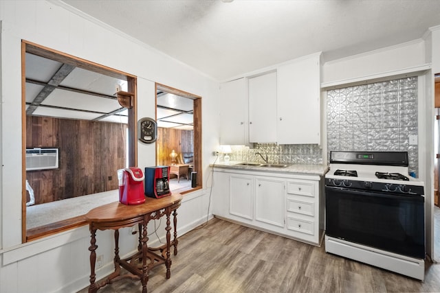 kitchen with tasteful backsplash, white cabinets, light wood-type flooring, sink, and white gas range oven