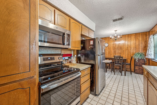 kitchen featuring a notable chandelier, decorative light fixtures, stainless steel appliances, wood walls, and light tile patterned floors