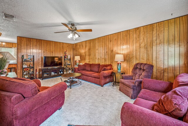 carpeted living room featuring wood walls, a textured ceiling, and ceiling fan