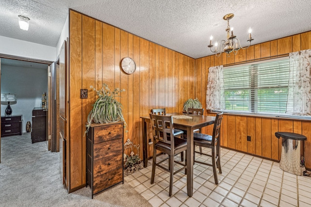 carpeted dining space with a textured ceiling, wood walls, and an inviting chandelier