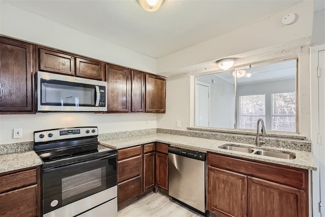 kitchen with dark brown cabinetry, sink, light stone counters, stainless steel appliances, and light hardwood / wood-style floors