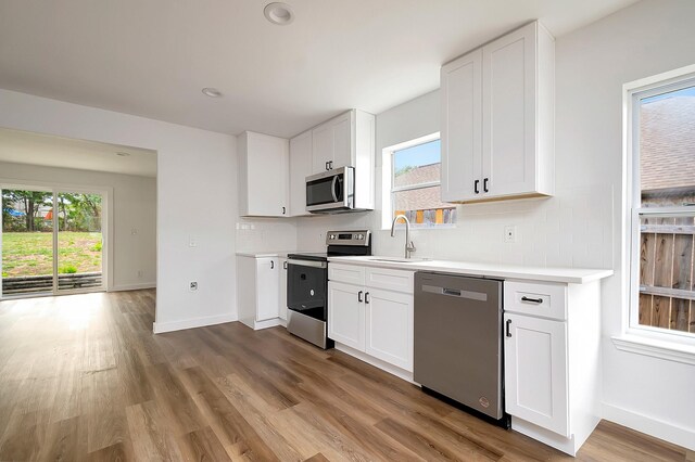 kitchen with a wealth of natural light, appliances with stainless steel finishes, light hardwood / wood-style floors, and white cabinetry