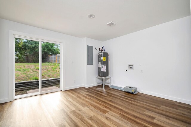 unfurnished room featuring light hardwood / wood-style floors, electric panel, and water heater