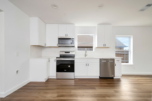 kitchen with white cabinetry, tasteful backsplash, stainless steel appliances, hardwood / wood-style floors, and sink