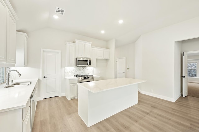 kitchen with appliances with stainless steel finishes, sink, white cabinets, backsplash, and a center island