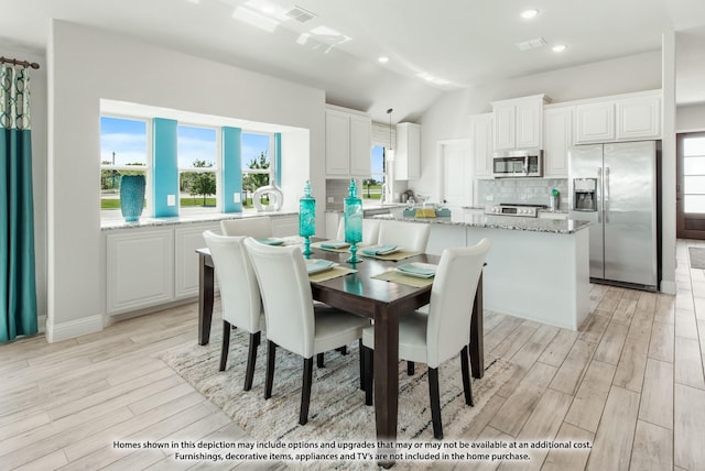 dining space featuring a healthy amount of sunlight, lofted ceiling, and light hardwood / wood-style floors