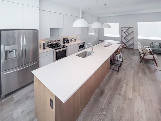 kitchen featuring white cabinetry, hanging light fixtures, stainless steel appliances, and an island with sink