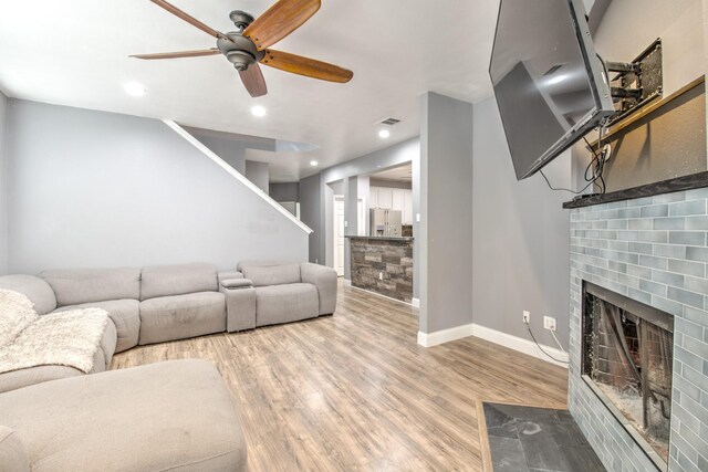 living room featuring wood-type flooring, a brick fireplace, and ceiling fan