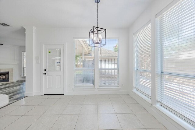 unfurnished dining area featuring a tiled fireplace, light tile patterned floors, and a chandelier