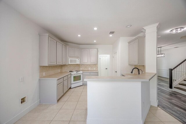 kitchen featuring decorative backsplash, kitchen peninsula, white appliances, light wood-type flooring, and decorative columns