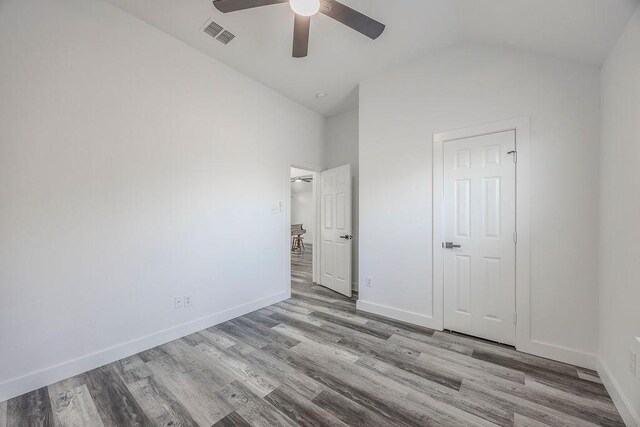 unfurnished bedroom with ceiling fan, wood-type flooring, a closet, and vaulted ceiling