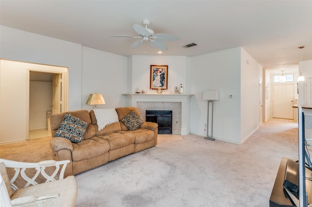 living room with ceiling fan, a tiled fireplace, and light carpet