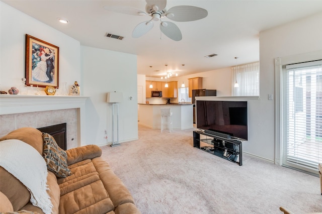 living room featuring a tiled fireplace, light colored carpet, and ceiling fan