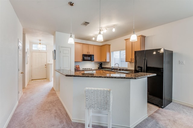 kitchen with decorative light fixtures, dark stone countertops, light brown cabinets, black appliances, and light carpet