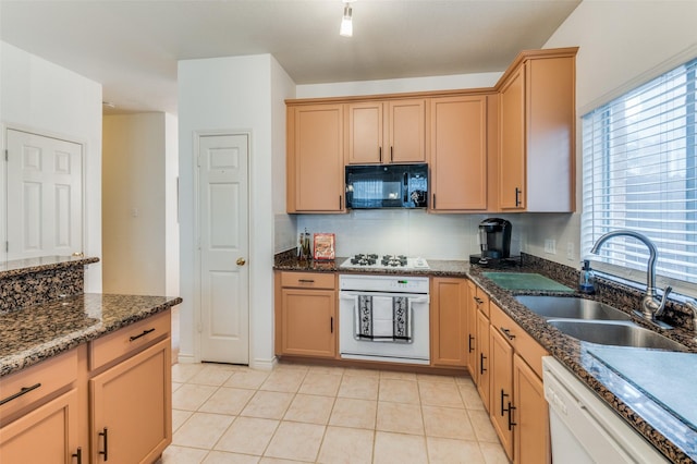 kitchen featuring white appliances, dark stone countertops, sink, and light tile patterned floors