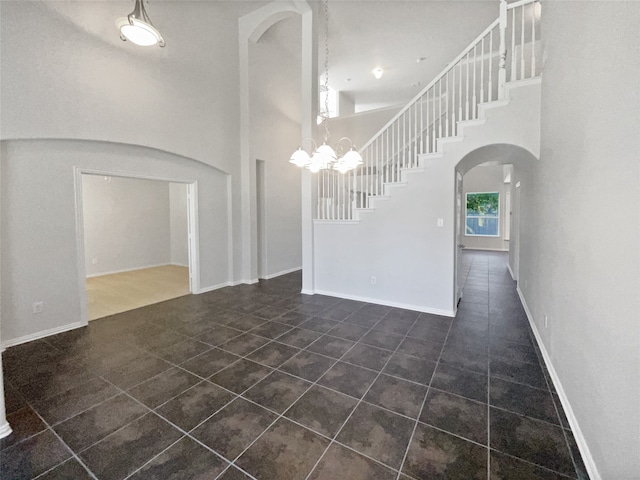 unfurnished room featuring a chandelier, dark tile patterned floors, and a towering ceiling