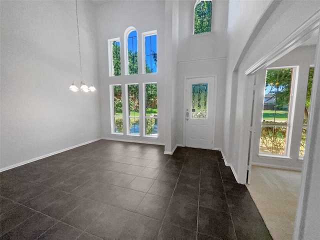 entryway with dark tile patterned floors, a notable chandelier, and a towering ceiling