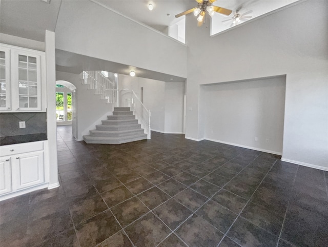 unfurnished living room with a high ceiling, ceiling fan, and dark tile patterned floors