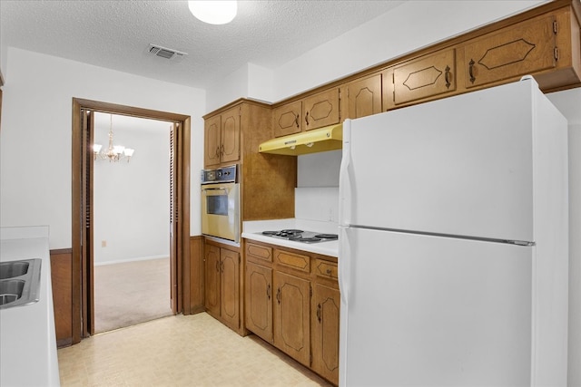 kitchen featuring gas cooktop, white refrigerator, light colored carpet, stainless steel oven, and a notable chandelier