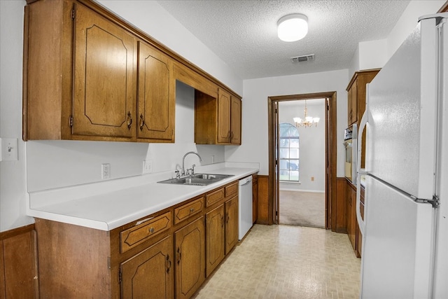 kitchen featuring white appliances, sink, an inviting chandelier, light colored carpet, and a textured ceiling