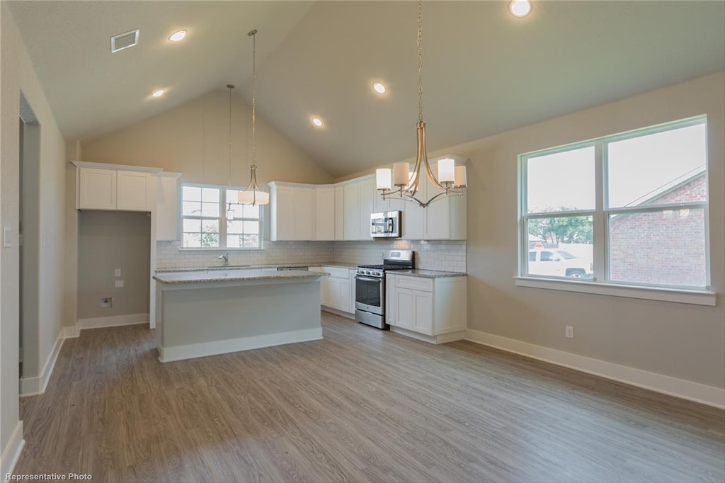 kitchen featuring decorative backsplash, white cabinets, appliances with stainless steel finishes, light wood-type flooring, and a center island