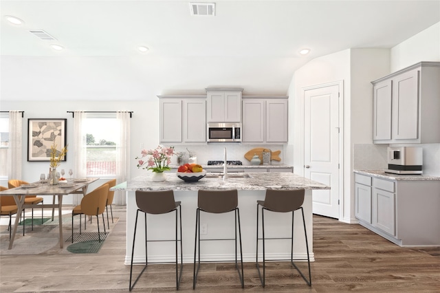 kitchen with light stone counters, hardwood / wood-style flooring, an island with sink, and gray cabinets