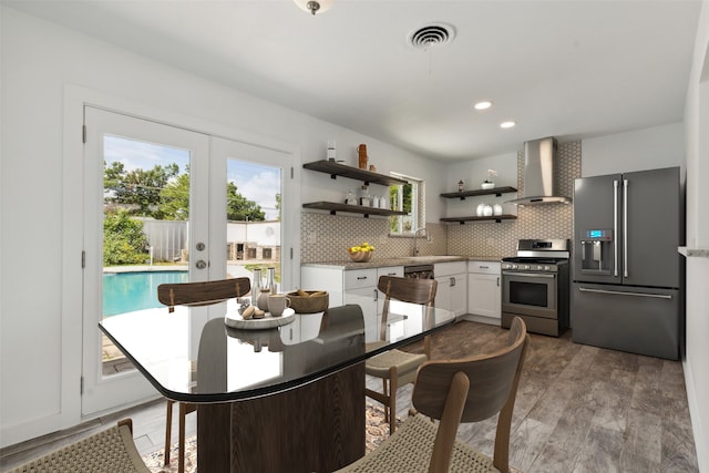 kitchen featuring light wood-type flooring, backsplash, wall chimney exhaust hood, stainless steel appliances, and white cabinets