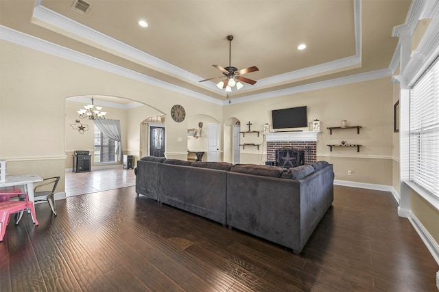 living room featuring dark hardwood / wood-style flooring, a brick fireplace, ceiling fan with notable chandelier, and a tray ceiling