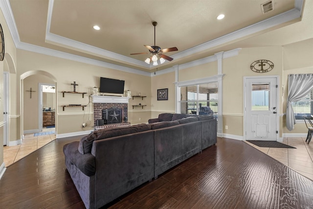 living room with a brick fireplace, hardwood / wood-style flooring, and a tray ceiling