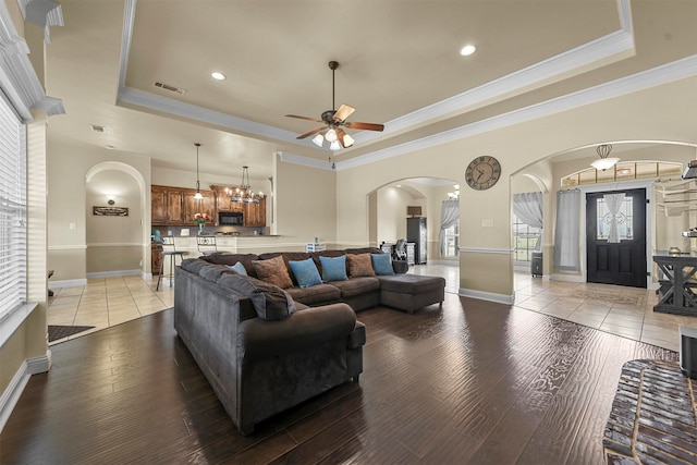 living room with crown molding, ceiling fan with notable chandelier, light wood-type flooring, and a tray ceiling