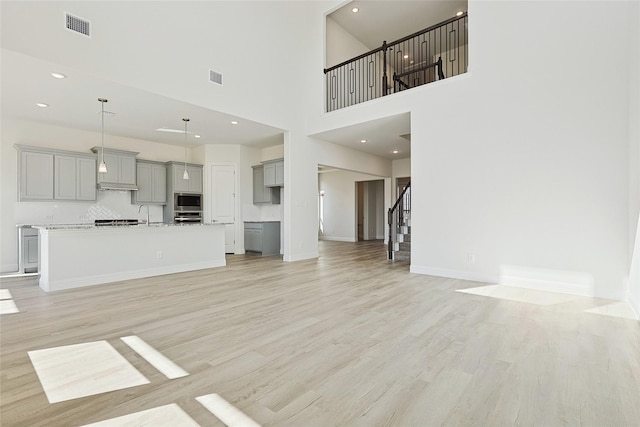 unfurnished living room with visible vents, light wood-style flooring, baseboards, and stairs