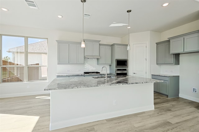 kitchen with appliances with stainless steel finishes, stone countertops, hanging light fixtures, and light hardwood / wood-style floors