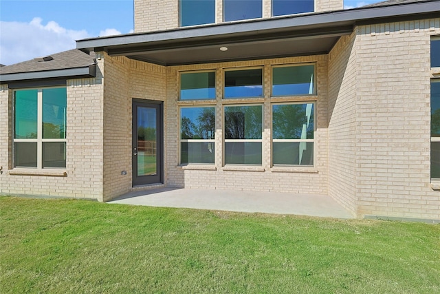 back of property with a patio area, a chimney, a lawn, and brick siding