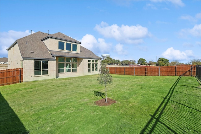 back of house with roof with shingles, brick siding, a lawn, and a fenced backyard