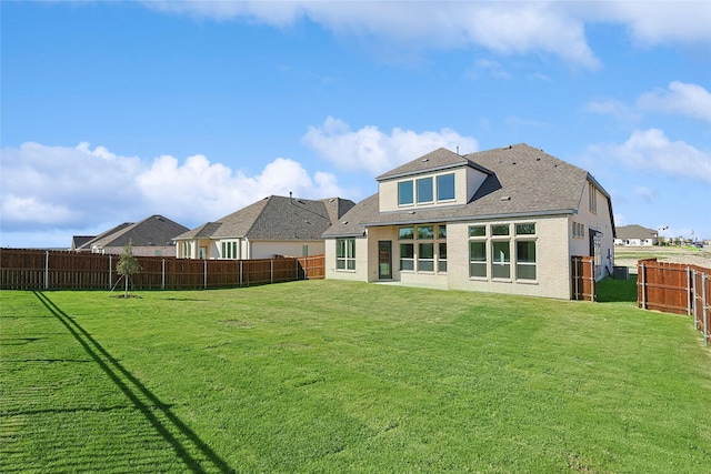 back of property featuring a yard, brick siding, and a fenced backyard