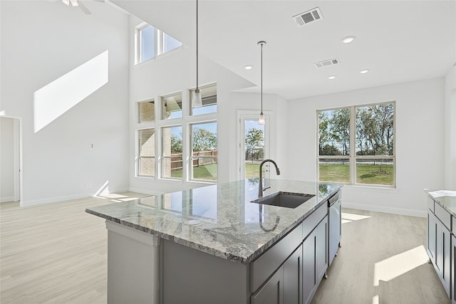 kitchen featuring visible vents, an island with sink, light stone counters, hanging light fixtures, and a sink