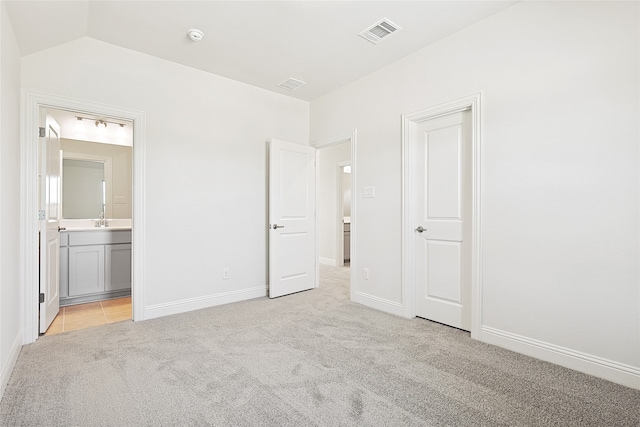 unfurnished bedroom with ensuite bath, lofted ceiling, and light colored carpet